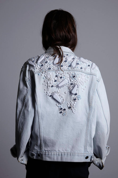 A person wearing the oversized Pinball Denim Bomber Jacket in 'Ice' blue. The jacket features a slouchy 80s-style cut with dropped shoulders and a striking pattern of oversized geometric ornaments across the back and sleeves.